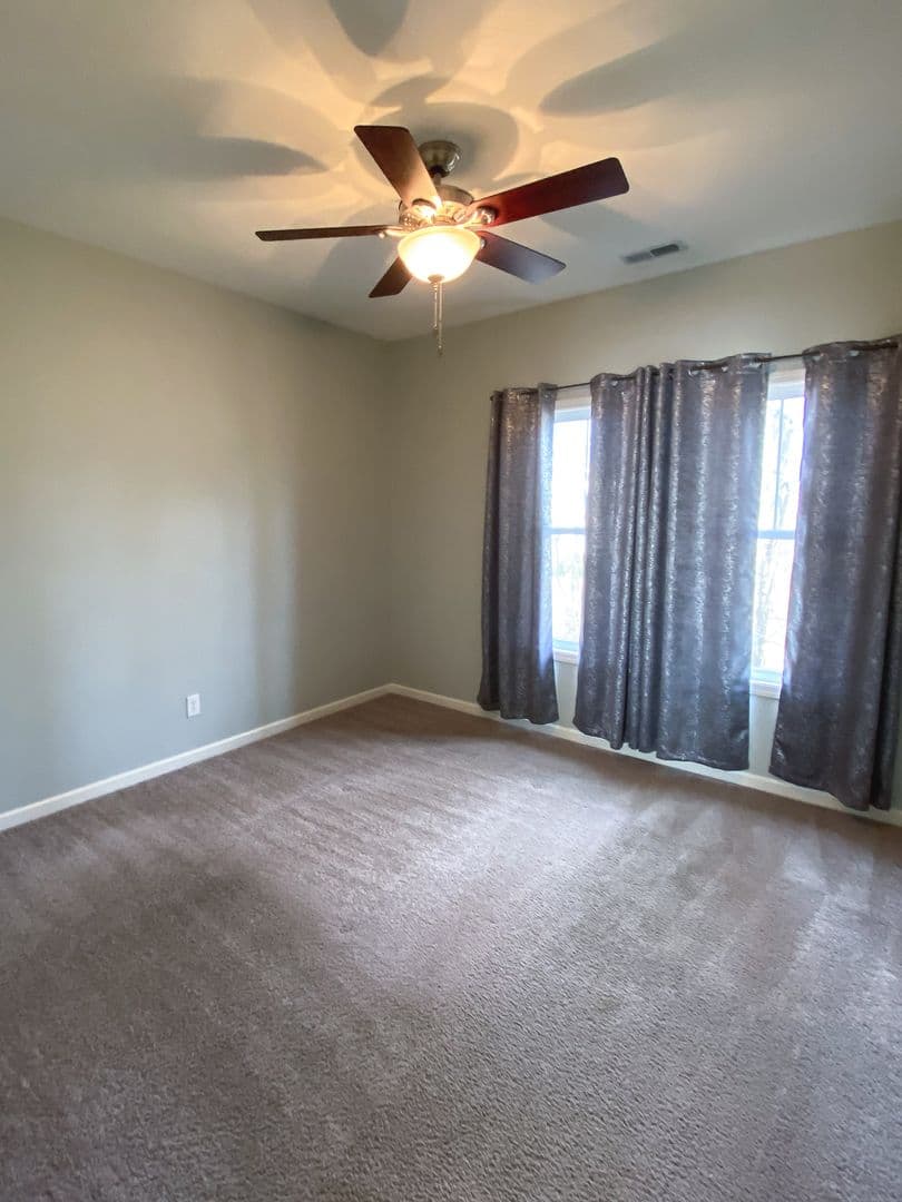 Carpeted bedroom with ceiling fan and floor-to-ceiling curtains